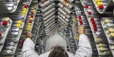 Photo of a pharmacist in a busy pharmacy, preparing a prescription with the help of automated dispensing equipment. The scene is shown from a view from bottom to top, focusing on the pharmacist’s precise work and the advanced equipment used for medication preparation. --chaos 13 --ar 4:3 Job ID: a2e63e94-2557-47ce-a4ea-88429d48966e